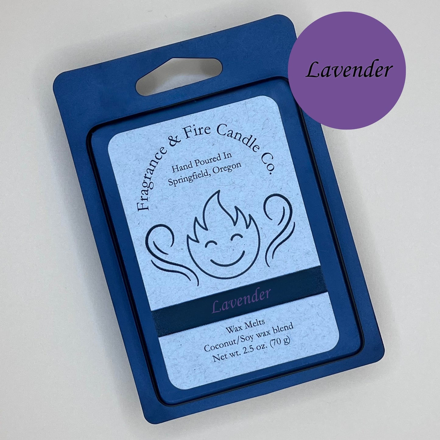 Black clamshell packaging for wax melts from Fragrance & Fire Candle Co., Springfield, Oregon. The packaging features a white label with a stylized flame logo, the text "Fragrance & Fire Candle Co. Hand Poured In Springfield, Oregon," and "Lavender" scent name. The label also includes the text "Wax Melts Coconut/Soy wax blend Net wt. 2.5 oz. (70 g)." A purple circle in the upper right corner says scent name.