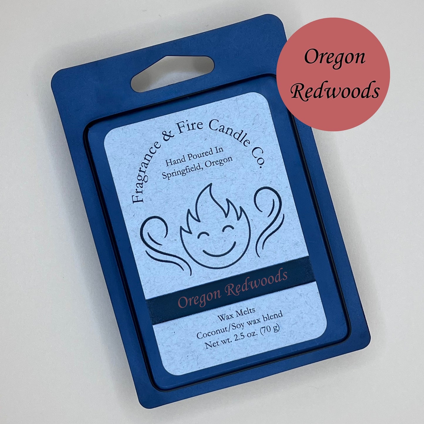 Black clamshell packaging for wax melts from Fragrance & Fire Candle Co., Springfield, Oregon. The packaging features a white label with a stylized flame logo, the text "Fragrance & Fire Candle Co. Hand Poured In Springfield, Oregon," and "Oregon Redwoods" scent name. The label also includes the text "Wax Melts Coconut/Soy wax blend Net wt. 2.5 oz. (70 g)." A burnt red circle in the upper right corner says scent name.