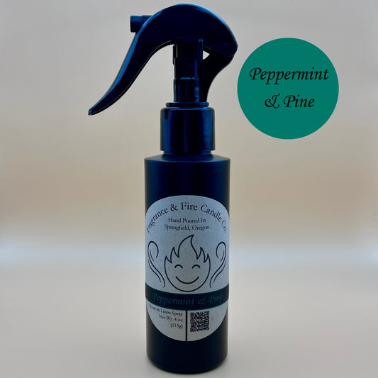 Black spray bottle from Fragrance & Fire Candle Co., Springfield, Oregon, with a black spray nozzle. The bottle has a white label with a stylized flame logo, the text "Fragrance & Fire Candle Co. Hand Poured In Springfield, Oregon," and "Display" scent name. The label also includes a QR code and the text "Room & Linen Spray Net Wt. 4 oz (113g)." A pine green circle in the upper right corner reads "Peppermint & Pine."