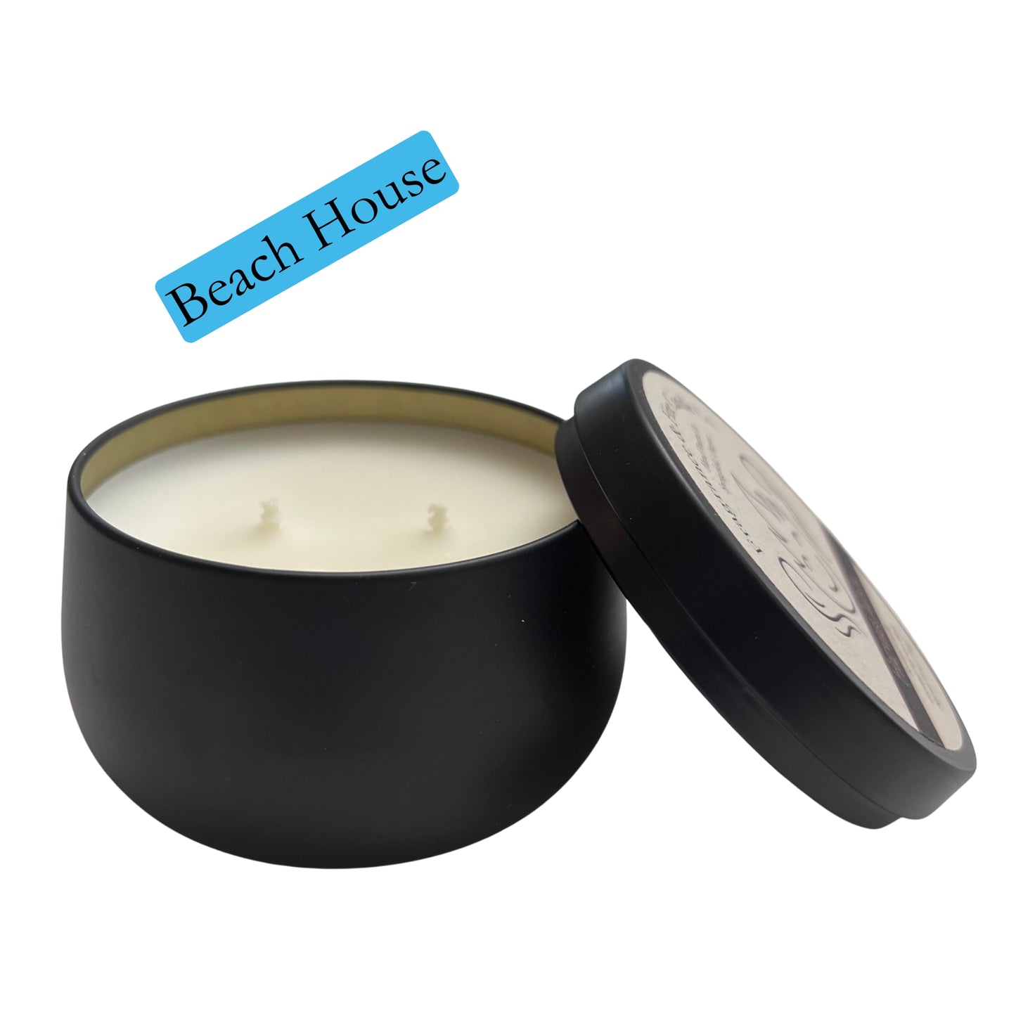 Fragrance & Fire Beach House candle. Black container with lid leaning on the side partially showing label with company logo. 2 wicks showing and gold lining of inside the container.