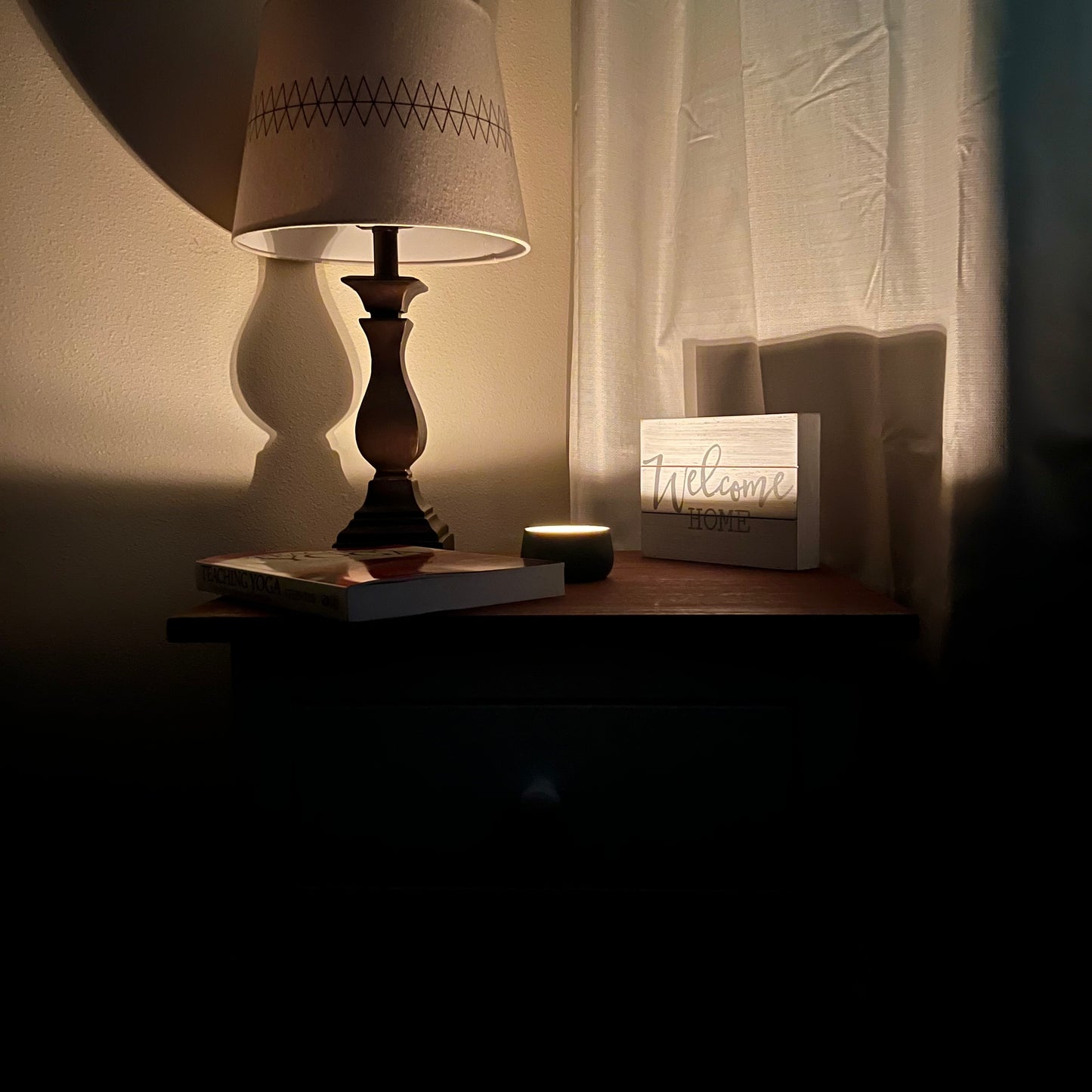 Dark room, lit candle on nightstand. Book, lamp, illumated by candle light.