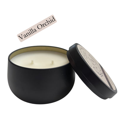 Fragrance & Fire Vanilla Orchid candle. Black container with lid leaning on the side partially showing label with company logo. 2 wicks showing and gold lining of inside the container.