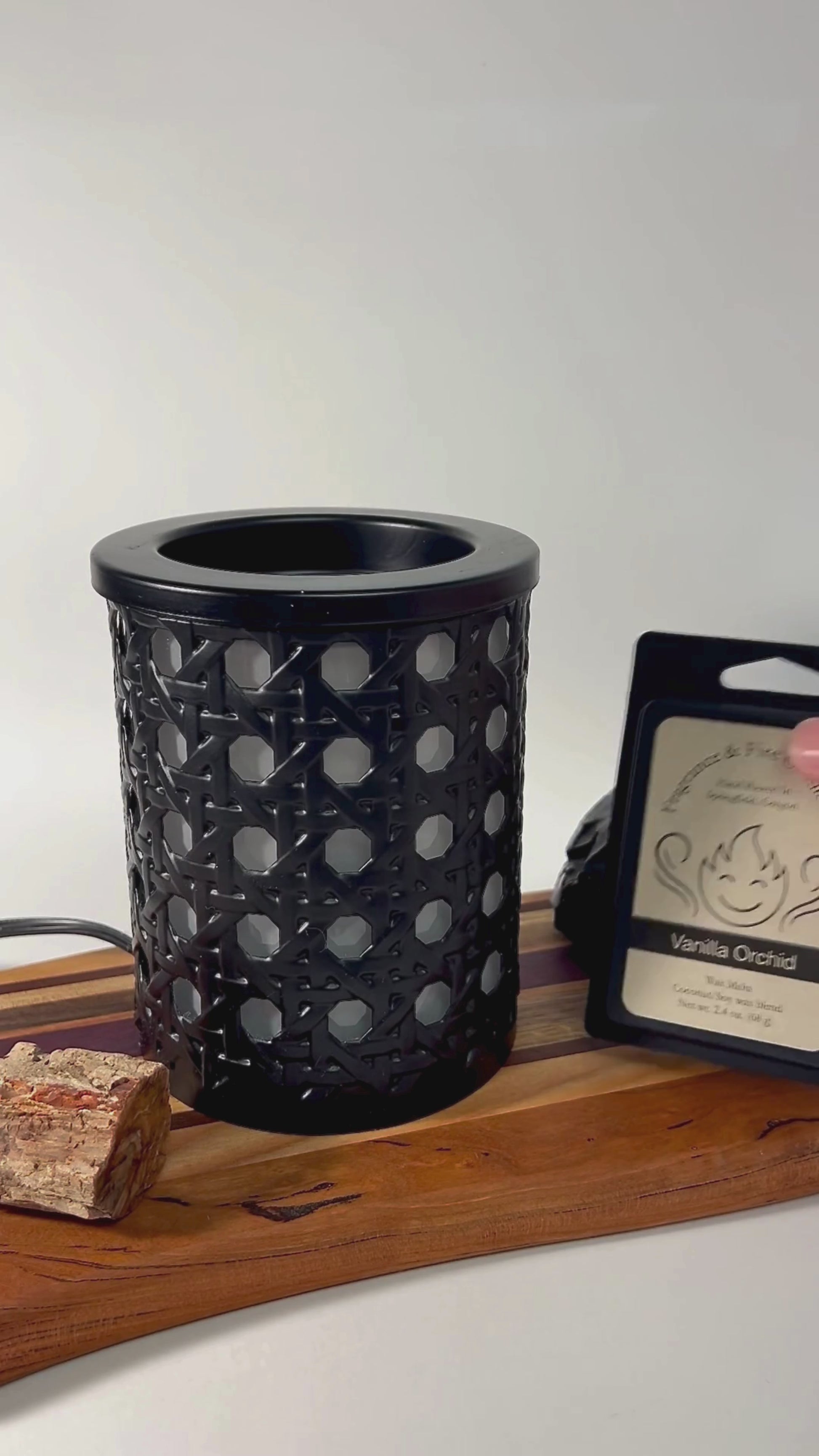 Video showcasing Wax Melts being opened, a wax cube placed into an electric wax melter, and the melter being turned on. The melter sits on a wooden board surrounded by rocks with a white background. The Fragrance & Fire Candle Co. logo and name appear at the end.